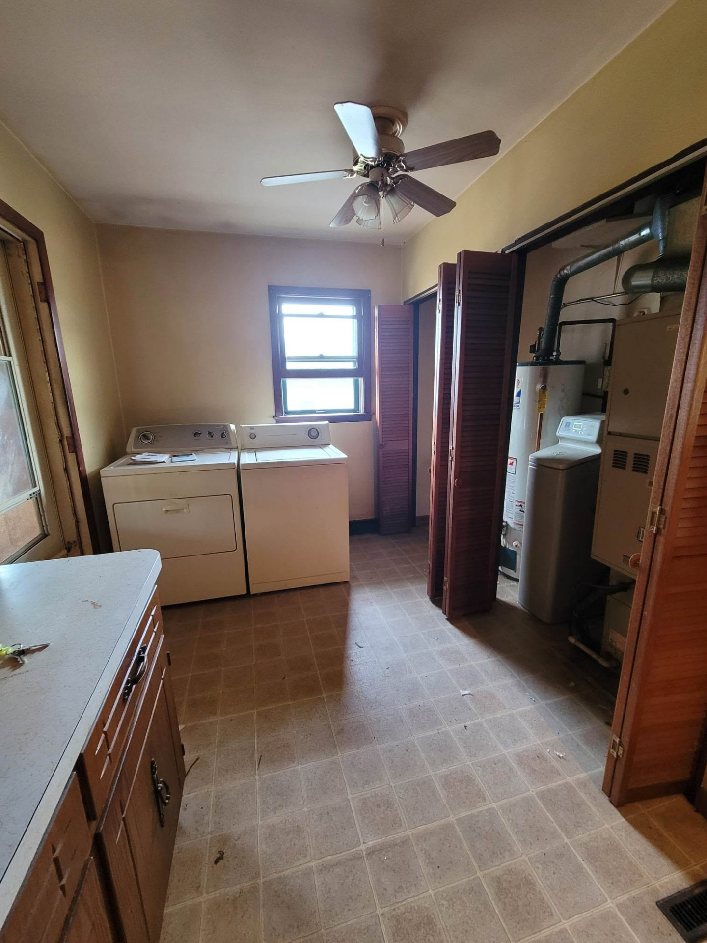 Before: dated laundry room with brown vinyl tile, dark louvered doors, and exposed utilities