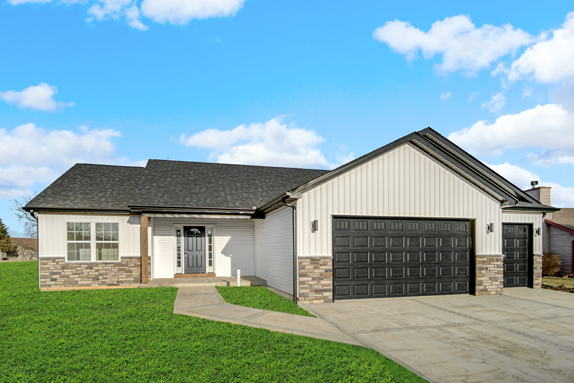 Front exterior of a newly built ranch spec home with board and batten siding, stone skirt, and a three-car garage