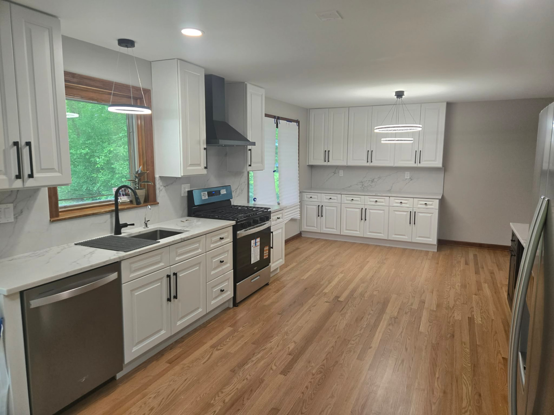 After: white raised-panel kitchen with quartz counters, full marble-look slab backsplash, matte black hardware, and red oak floors