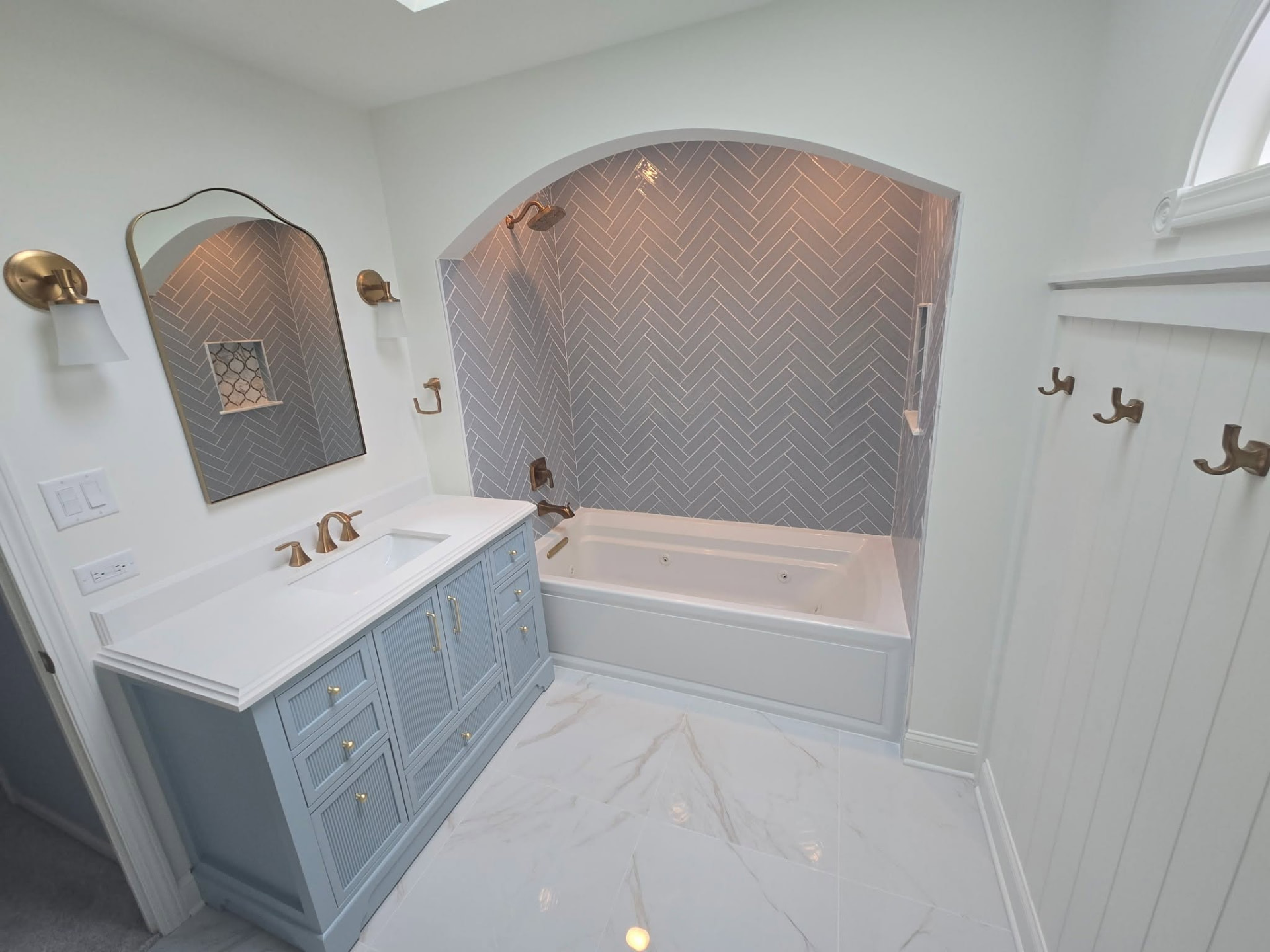 After: remodeled Lockport bathroom with blue vanity, brass fixtures, and arched herringbone tile tub alcove