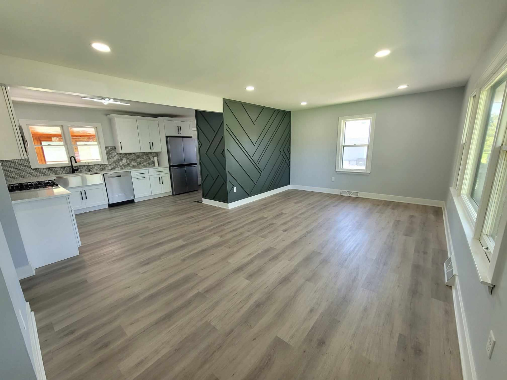 After: open front room with recessed lighting, luxury vinyl plank floors, and a green slat accent wall