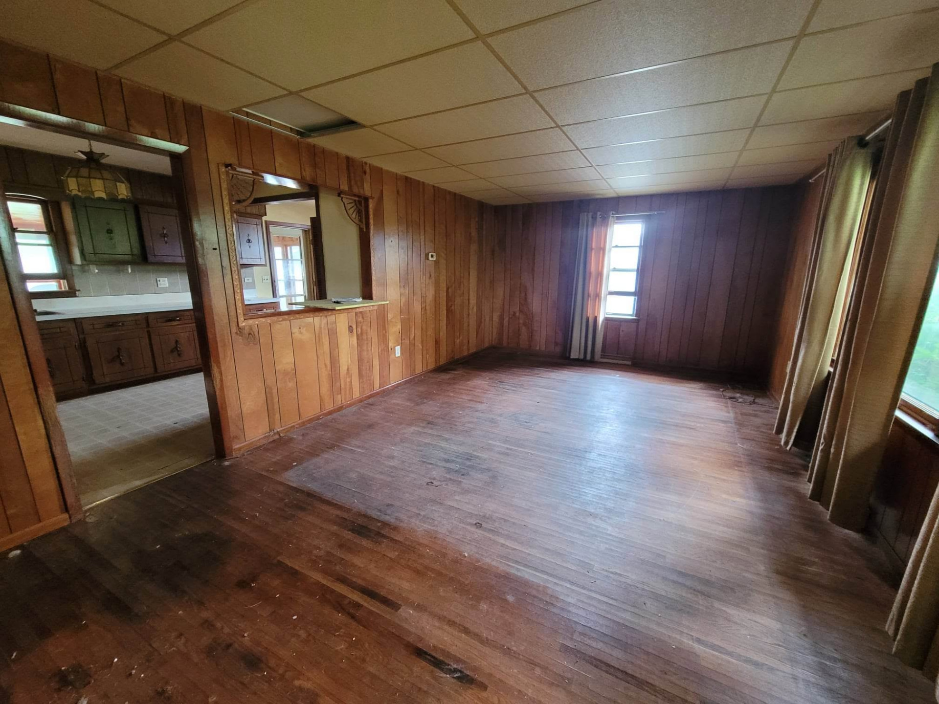 Before: wood-paneled front room with drop ceiling and worn hardwood floors