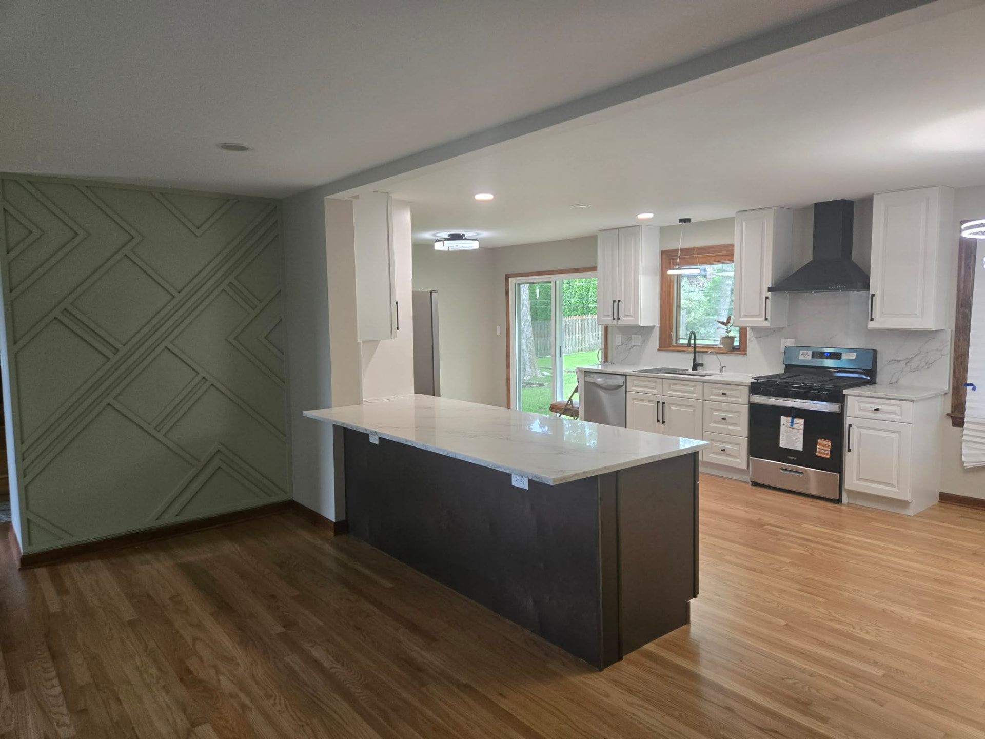 After: open concept with a large quartz-topped island, dark stained base, and custom sage green geometric slat wall
