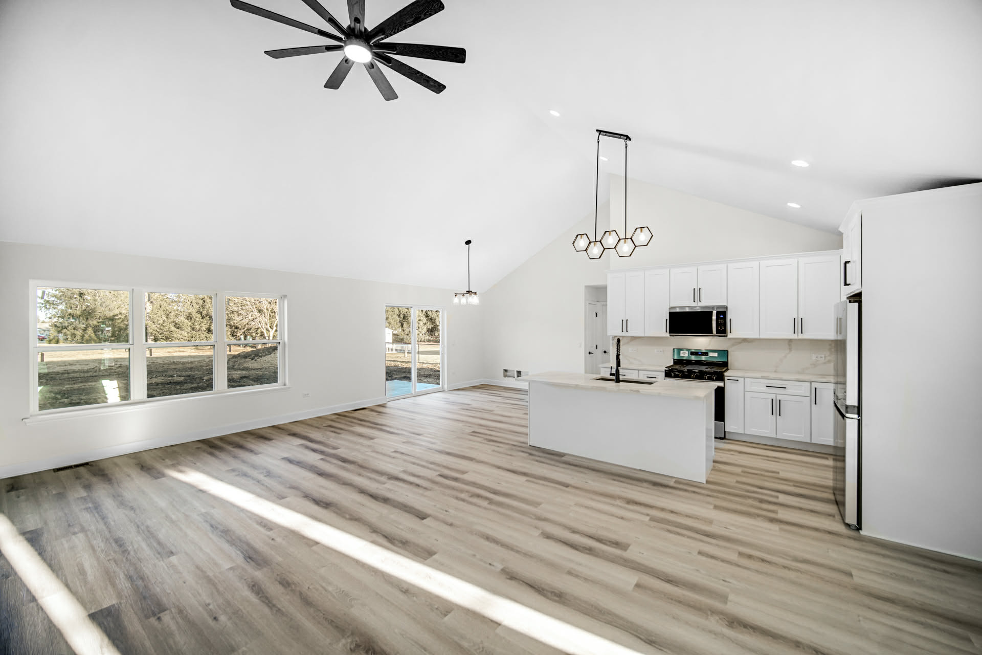 Vaulted open-concept great room with luxury vinyl plank flooring looking toward the white kitchen