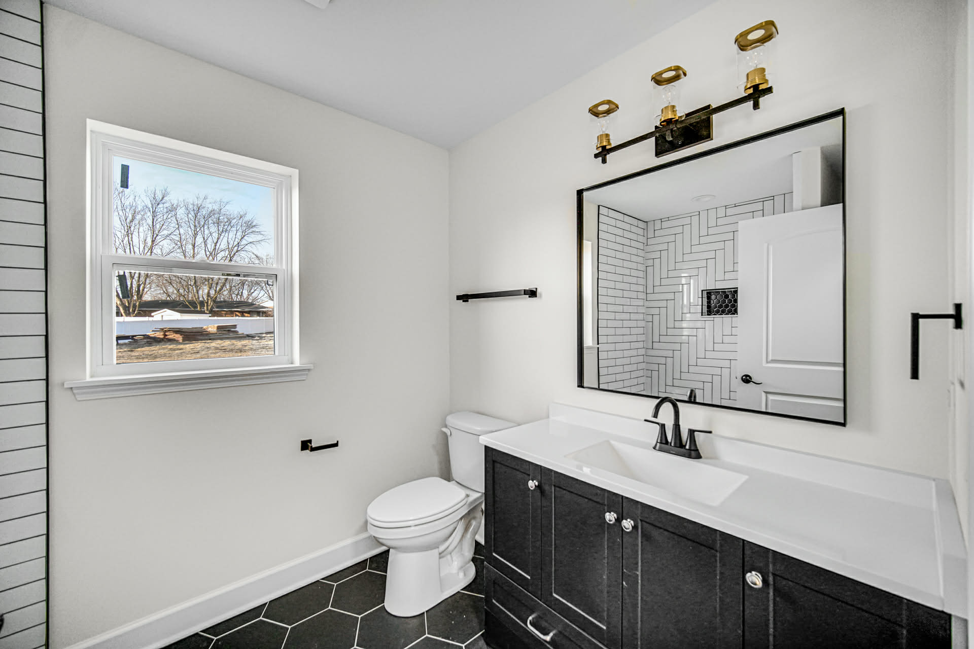 Hall bathroom with herringbone subway tile shower, black vanity, and hex tile floor