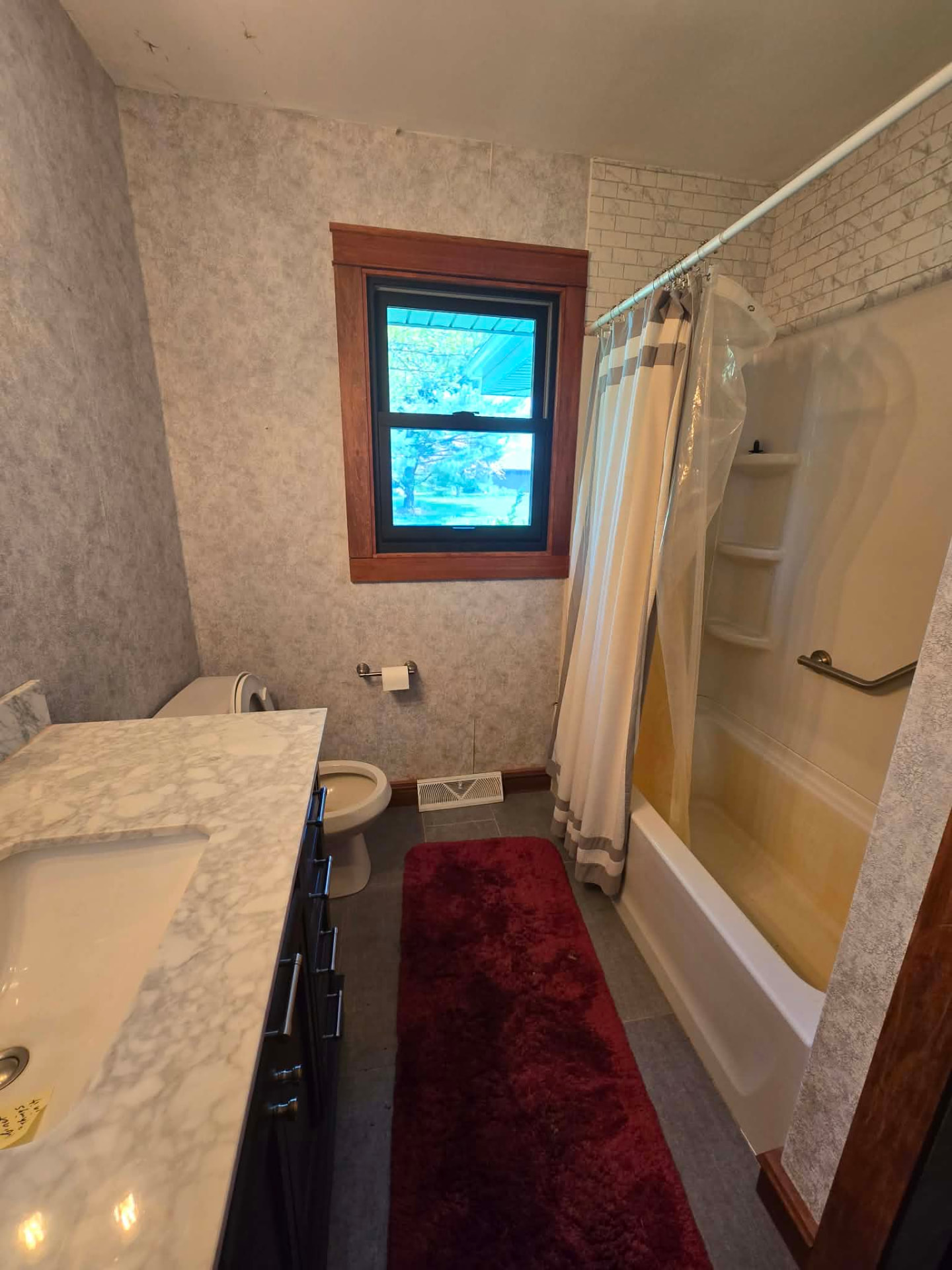 Before: original alcove tub with yellowed fiberglass surround, grab bar, and peel-and-stick brick backsplash