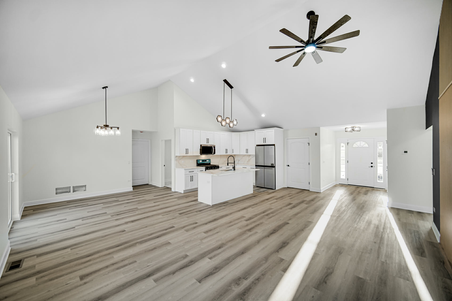 Wide view of the open plan from the entry with vaulted ceilings and modern light fixtures