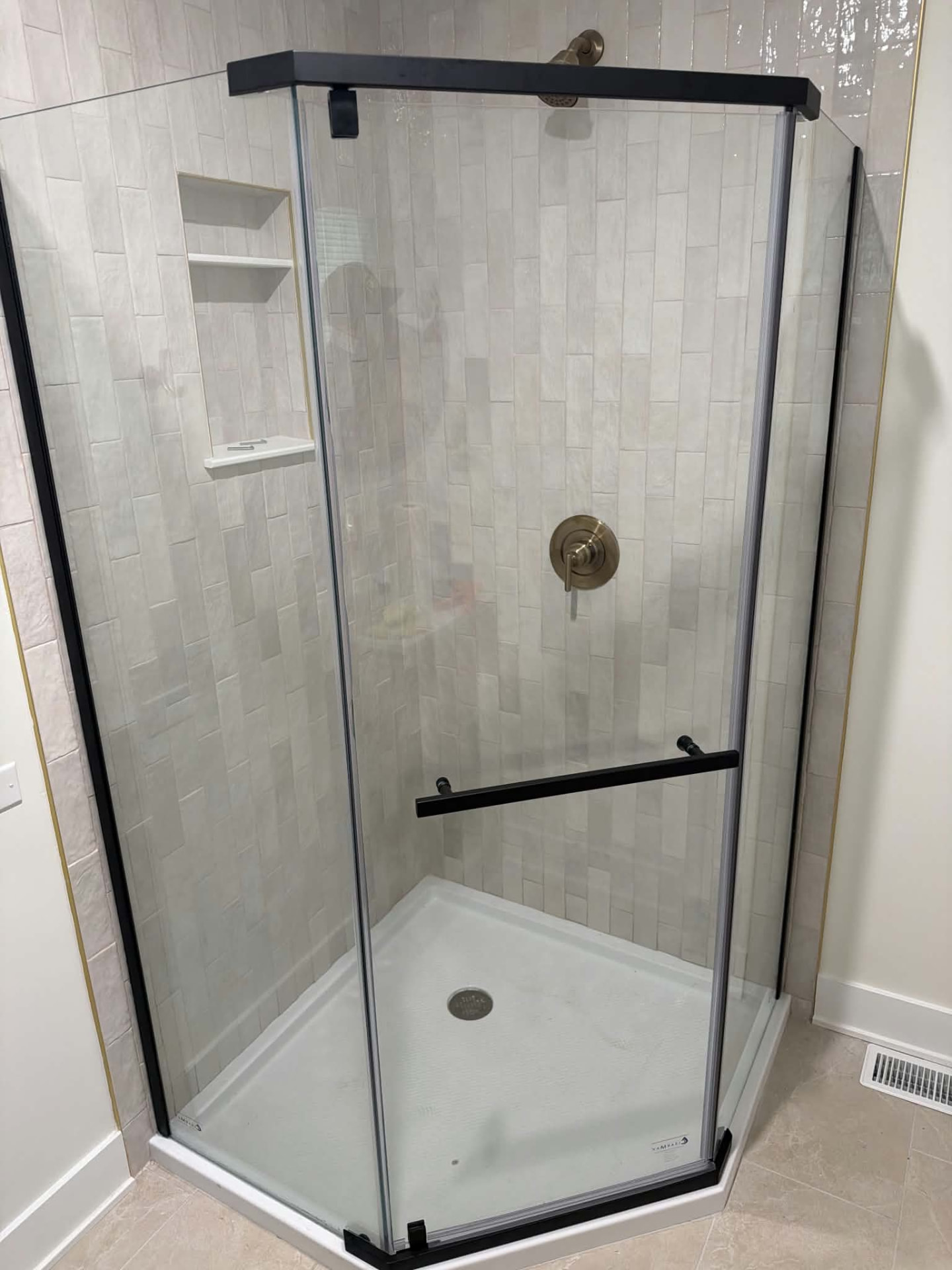 After: neo-angle glass shower with cream vertical tile walls, built-in niche shelving, matte black hardware, and brushed brass trim