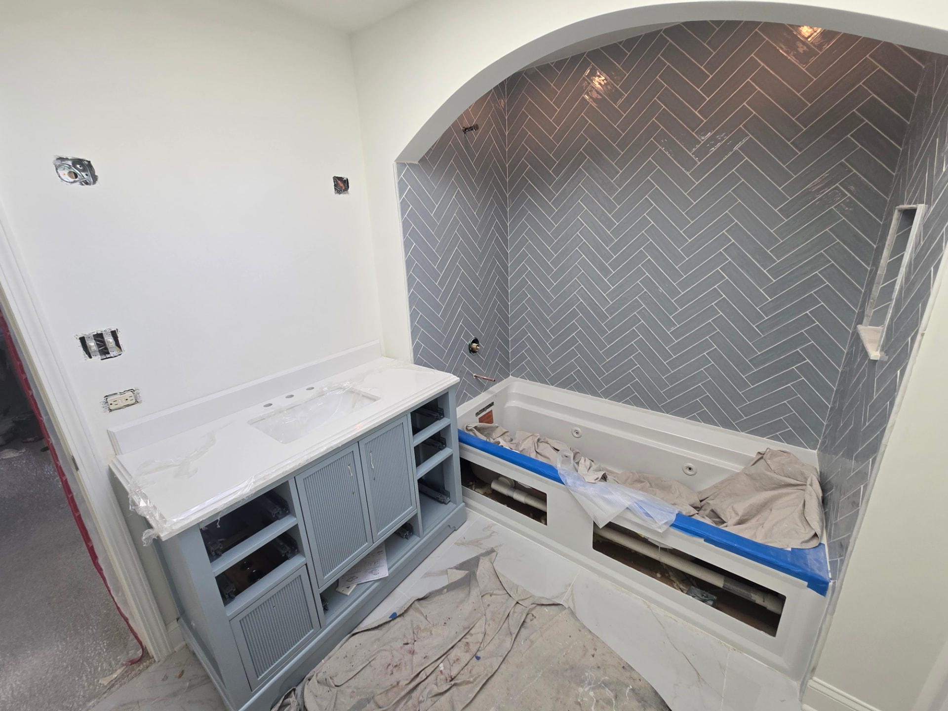 Blue bathroom vanity installed during Lockport bathroom renovation with countertop in place, herringbone tile completed, and tub protected while room is still under construction
