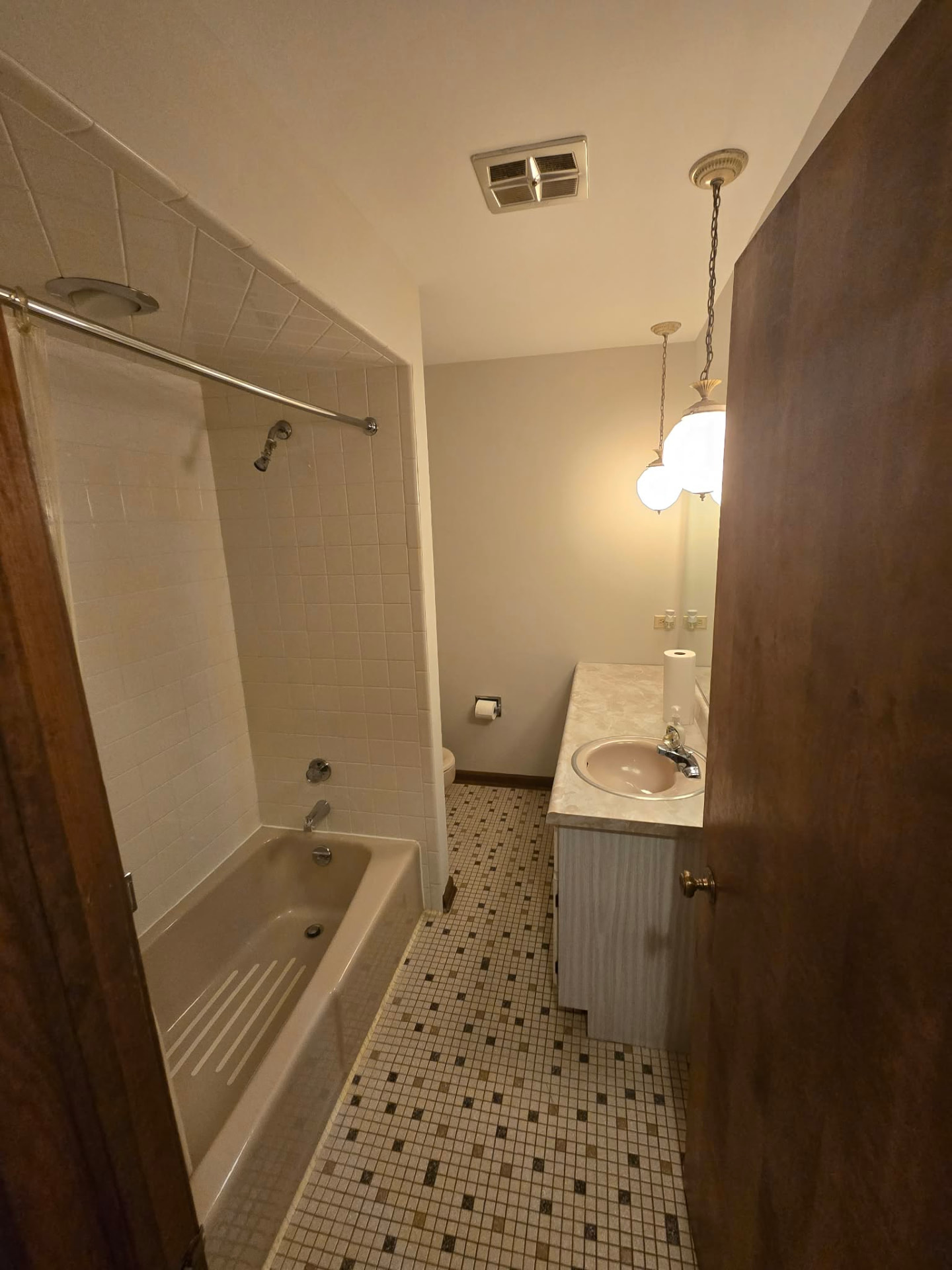 Before: narrow guest bathroom with a dated tub-shower alcove, mosaic tile floor, and laminate vanity with a pink sink
