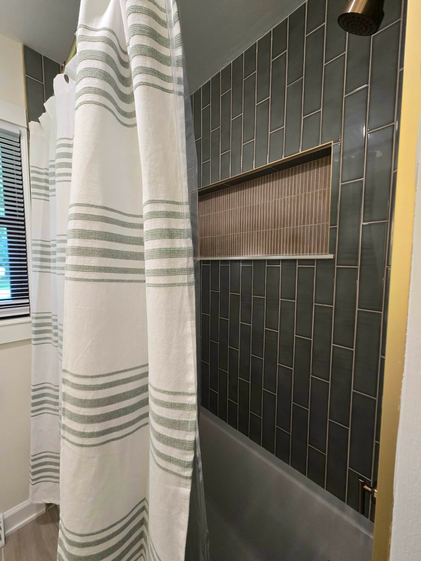 After: new tub with a vertical stacked deep green tile surround, brass-trimmed niche in fluted tile, and brass shower fittings