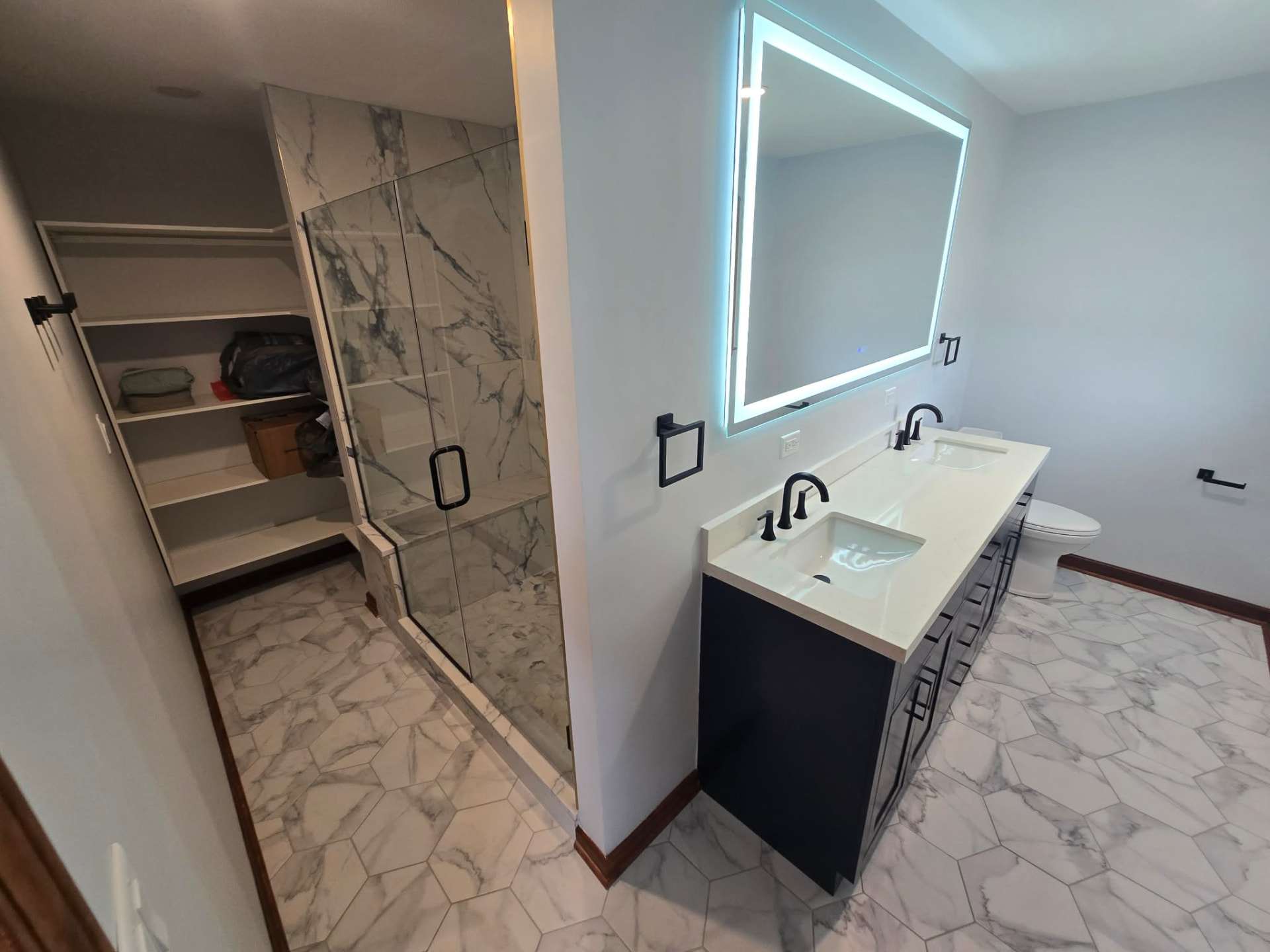 After: reframed primary bath with a new glass walk-in shower in marble tile, hex marble floor, LED mirror, navy double vanity, and a new walk-in closet