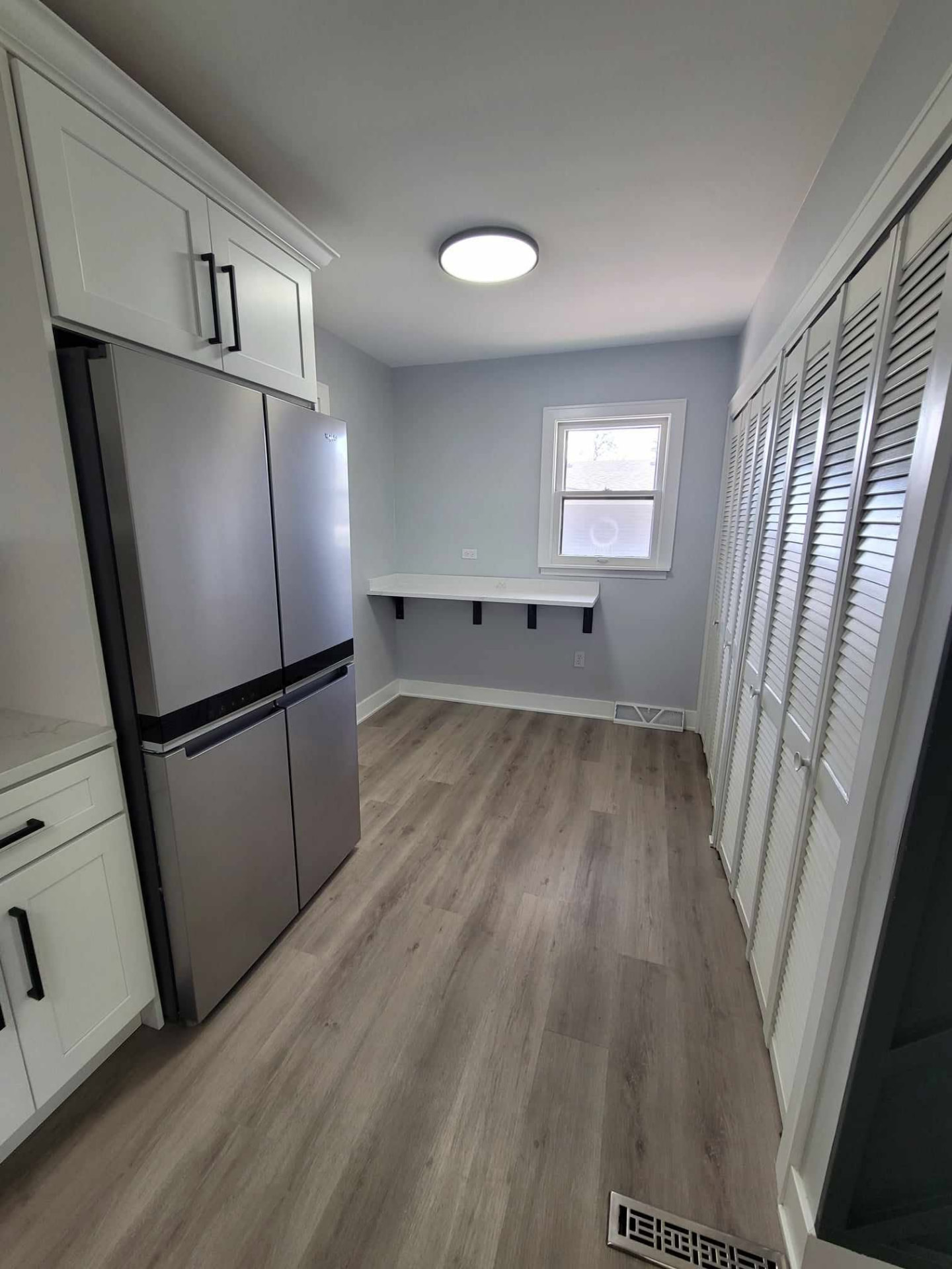 After: bright laundry and mud room with white cabinetry, quartz shelf with hooks, and new louvered closet doors