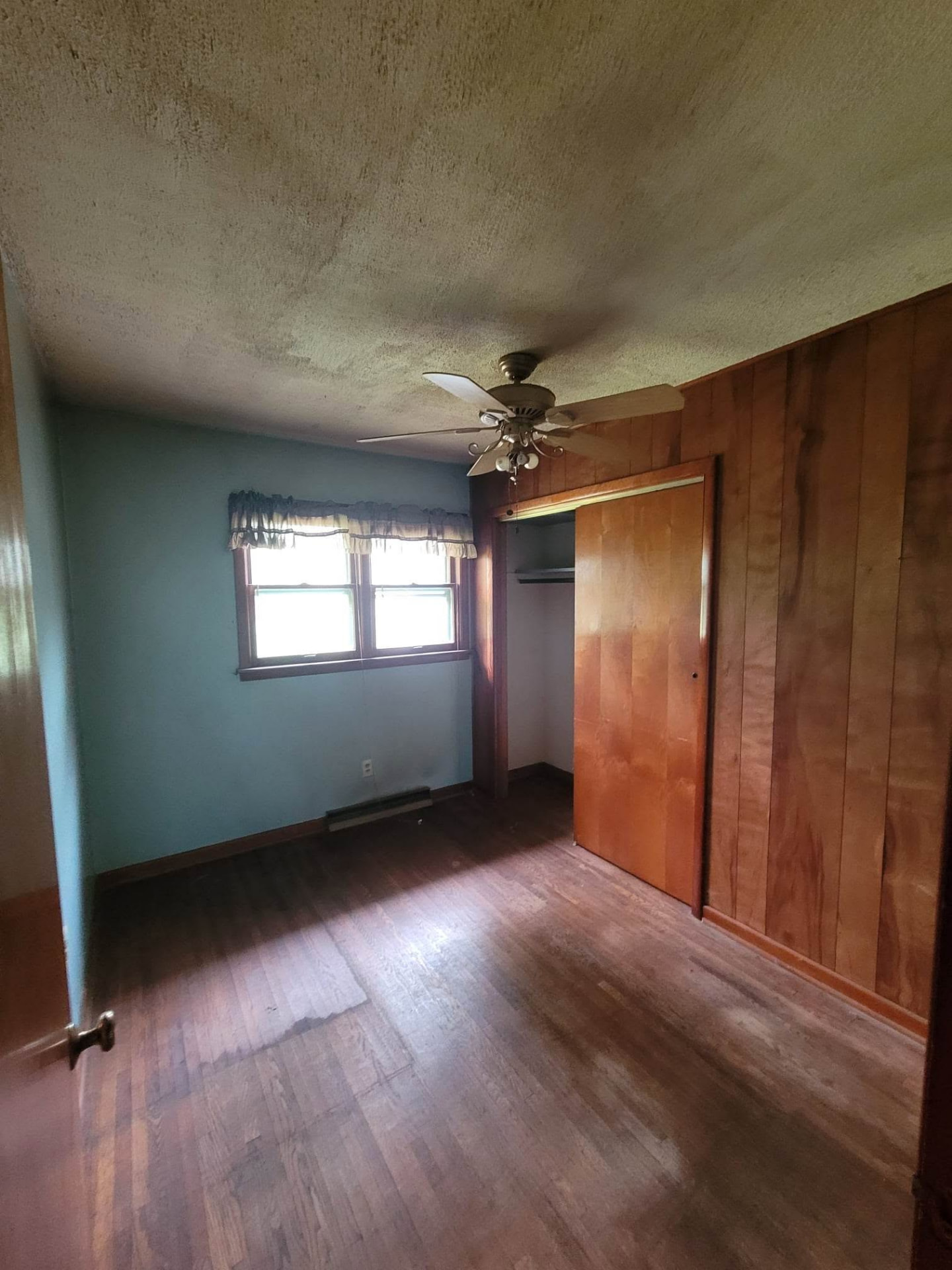 Before: dated bedroom with wood paneling, textured ceiling, and worn hardwood floors