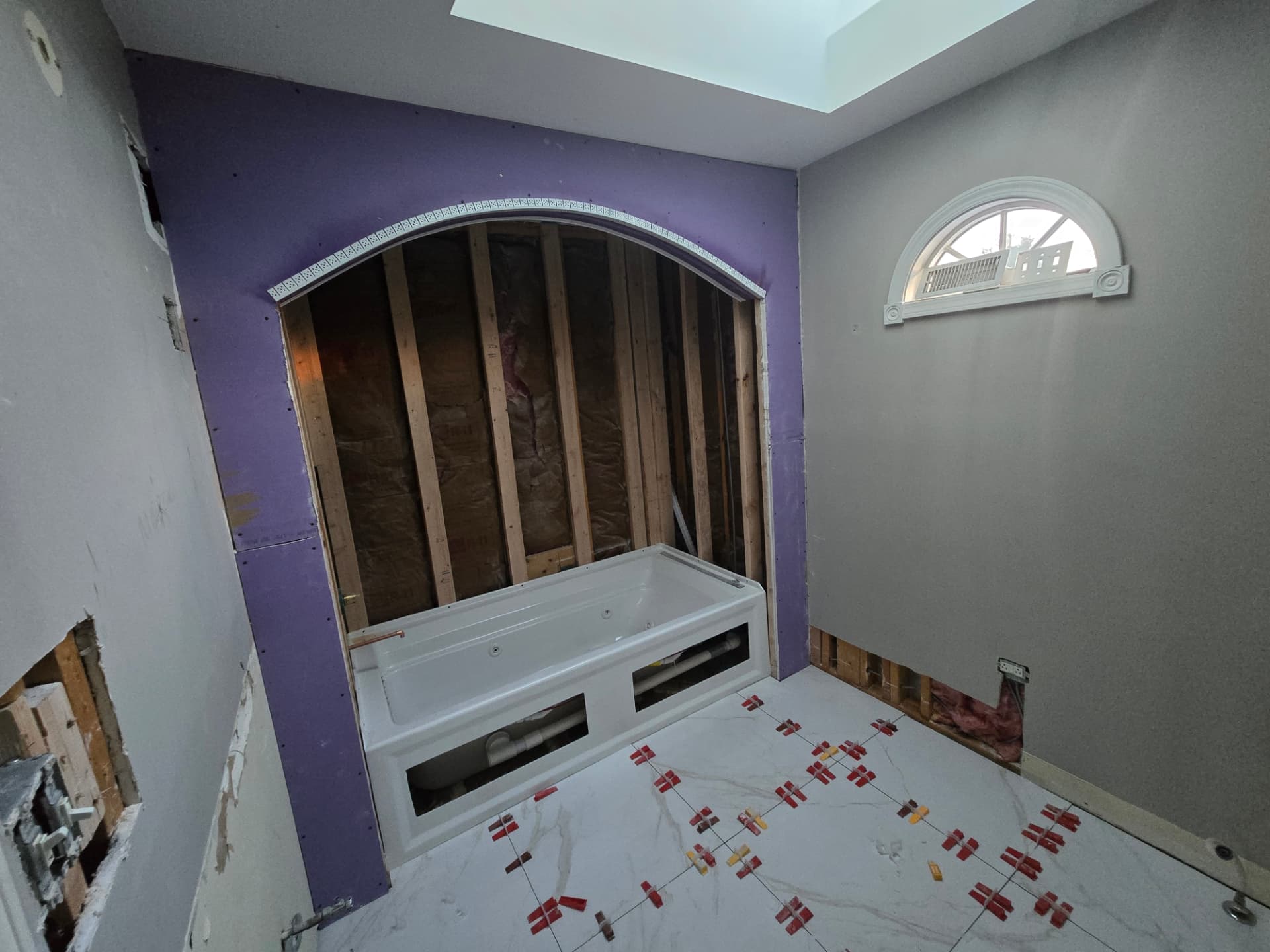 Large format porcelain floor tile installation during Lockport bathroom remodel with purple moisture resistant wall board around the arched tub alcove and leveling clips on the floor