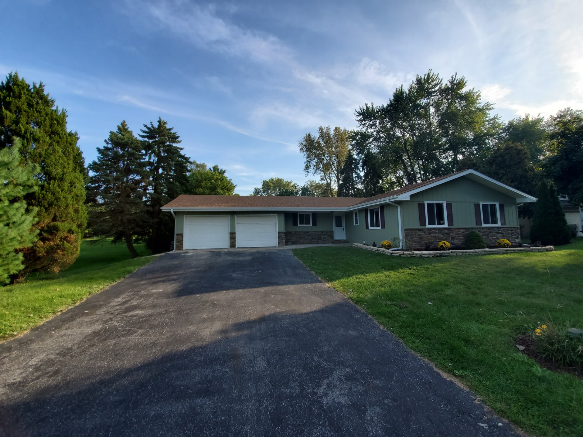 After: sage green siding, new stone wainscot, fresh landscaping beds, and updated windows