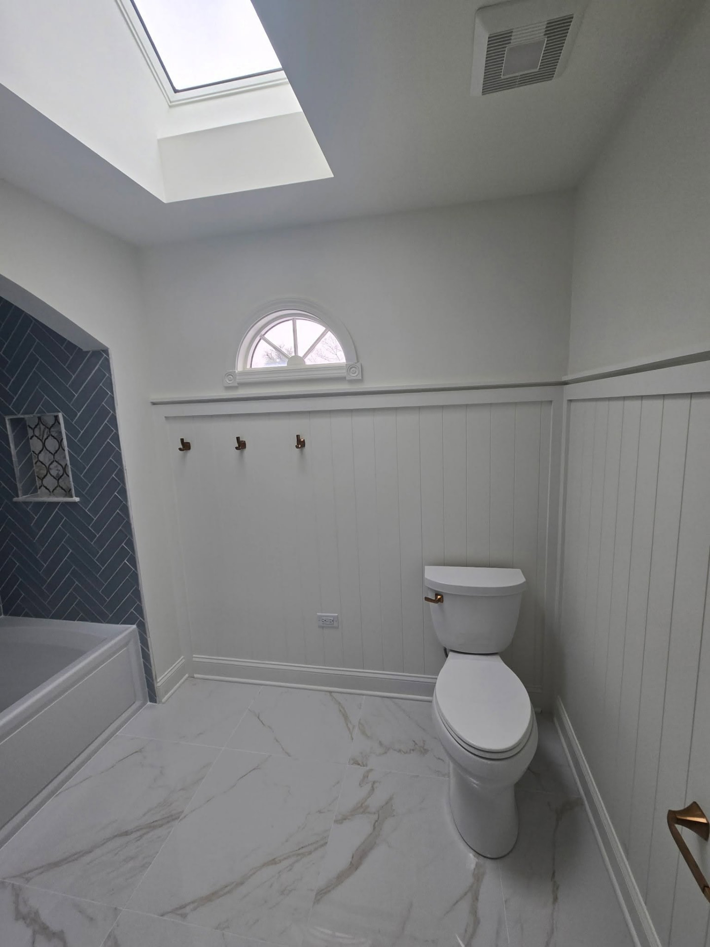 White beadboard wainscoting, arched window, and marble-look porcelain floor tile