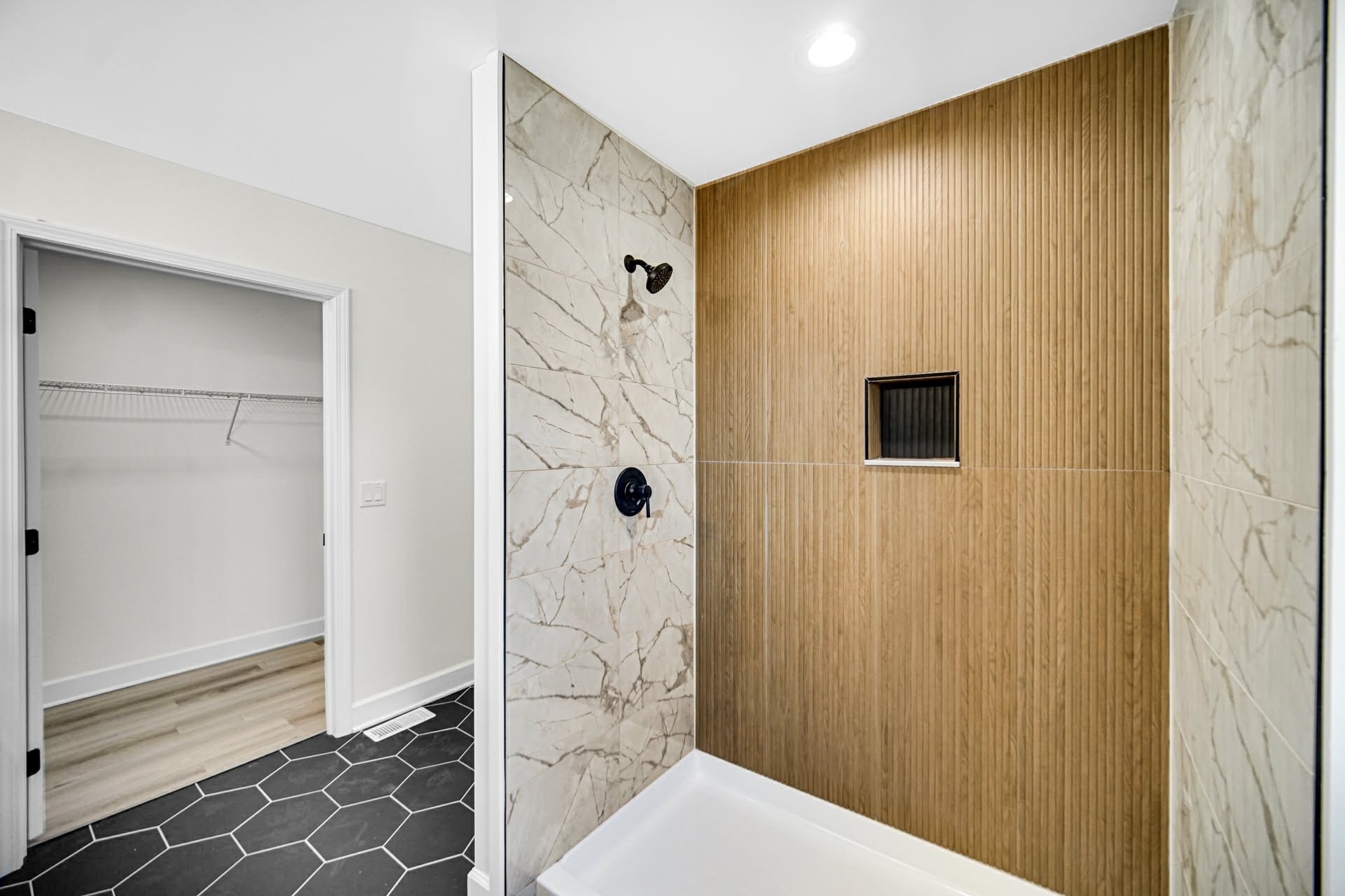 Primary walk-in shower with marble-look tile and a fluted oak accent wall