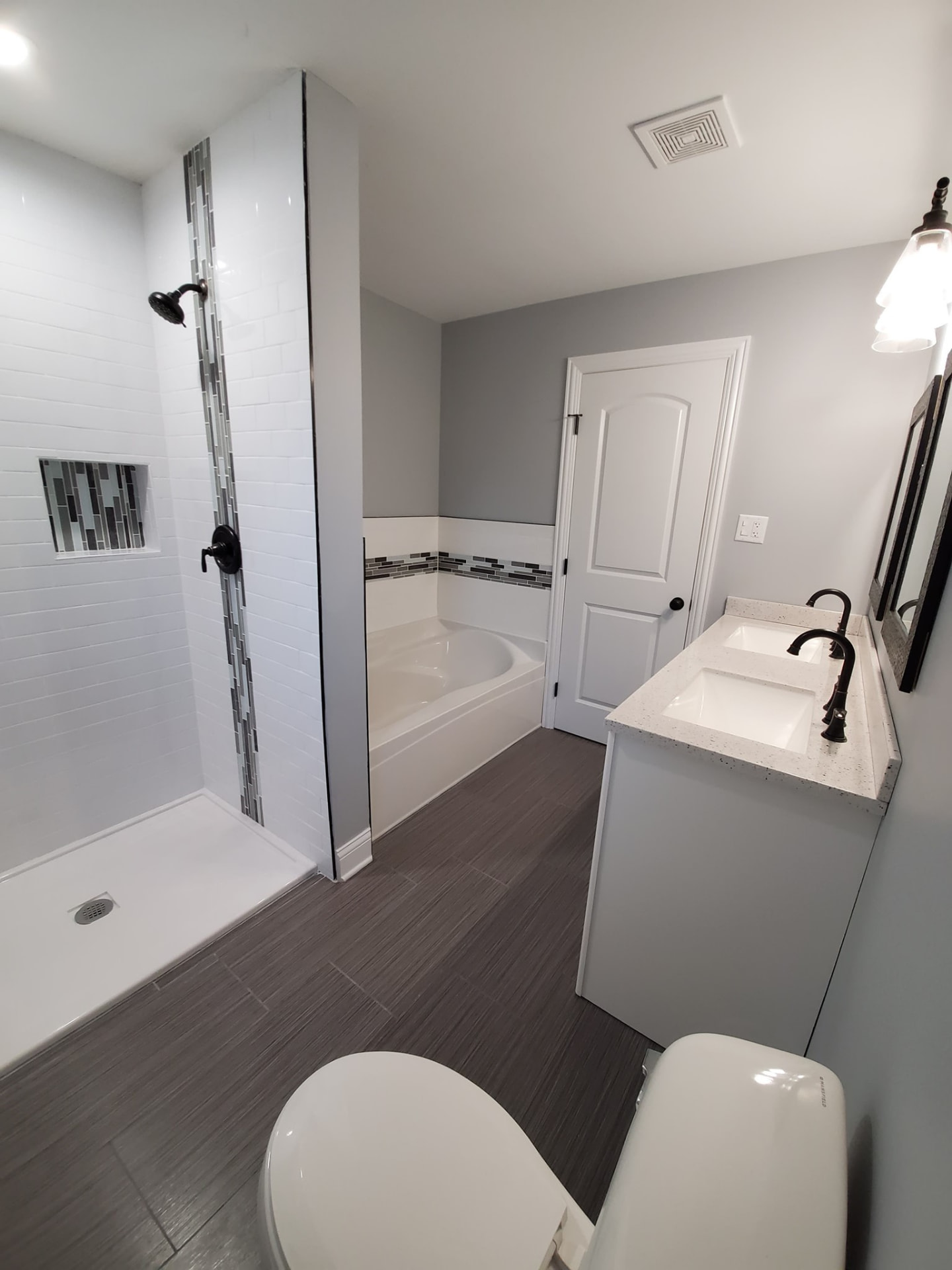 After: tiled walk-in shower with mosaic inlay, soaking tub, and double quartz vanity