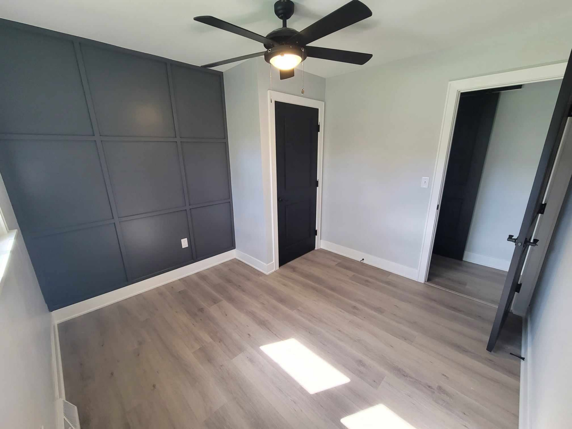 After: bedroom with charcoal grid trim accent wall, black doors, and new vinyl plank flooring