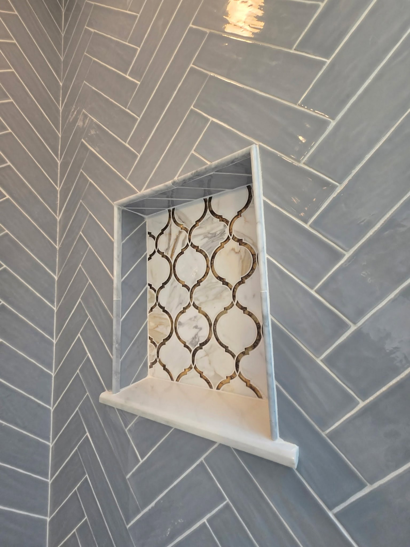 Custom marble shower niche with arabesque mosaic inset in blue herringbone tile