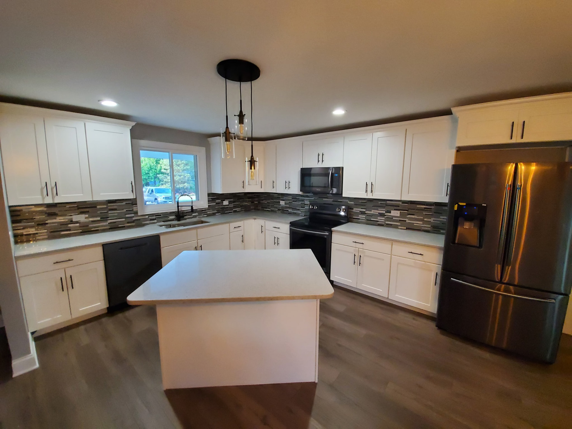 After: white shaker kitchen with quartz island, glass mosaic backsplash, and stainless appliances