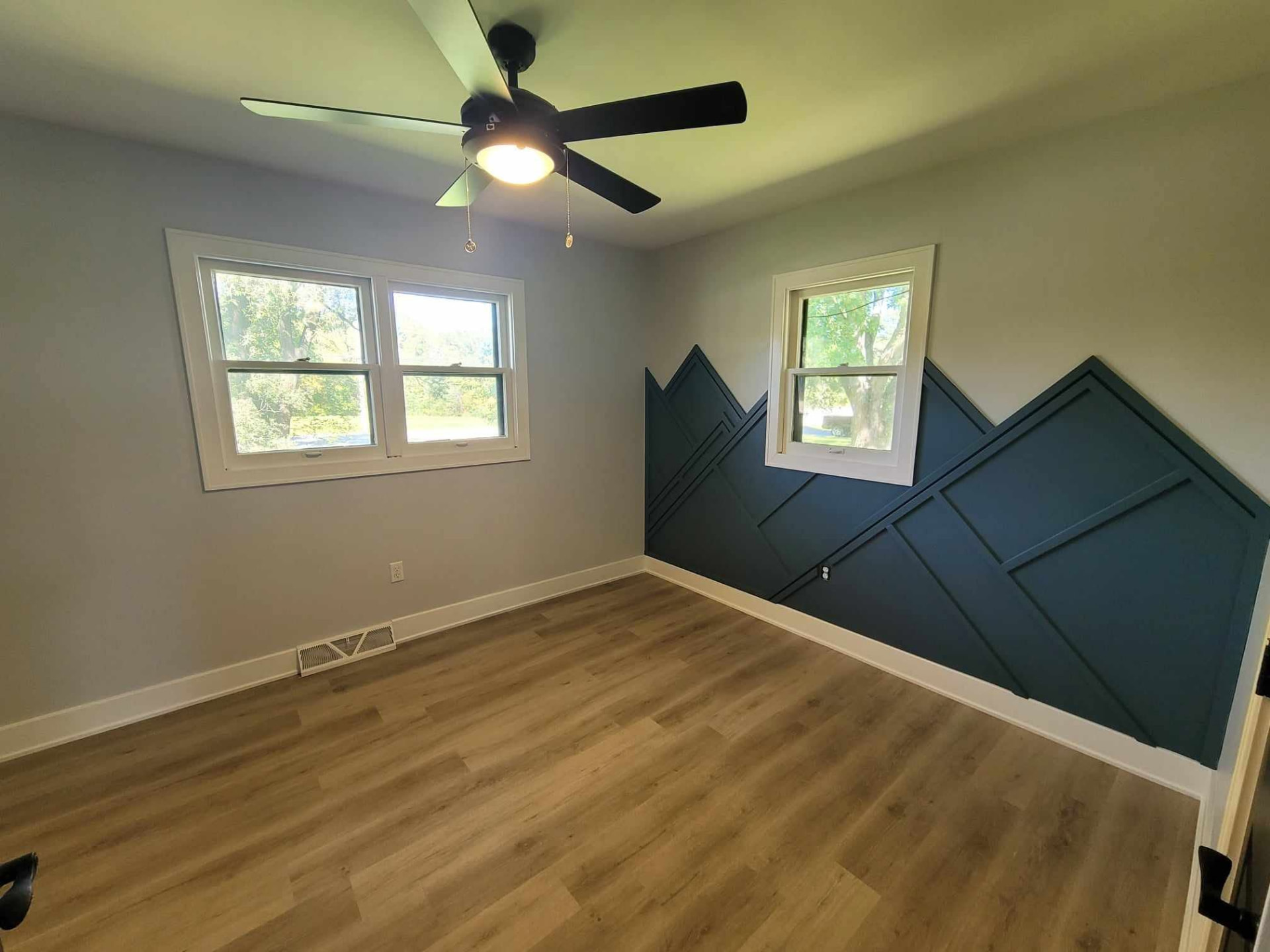 After: bedroom with custom navy mountain trim accent wall, new windows, and warm vinyl plank floors